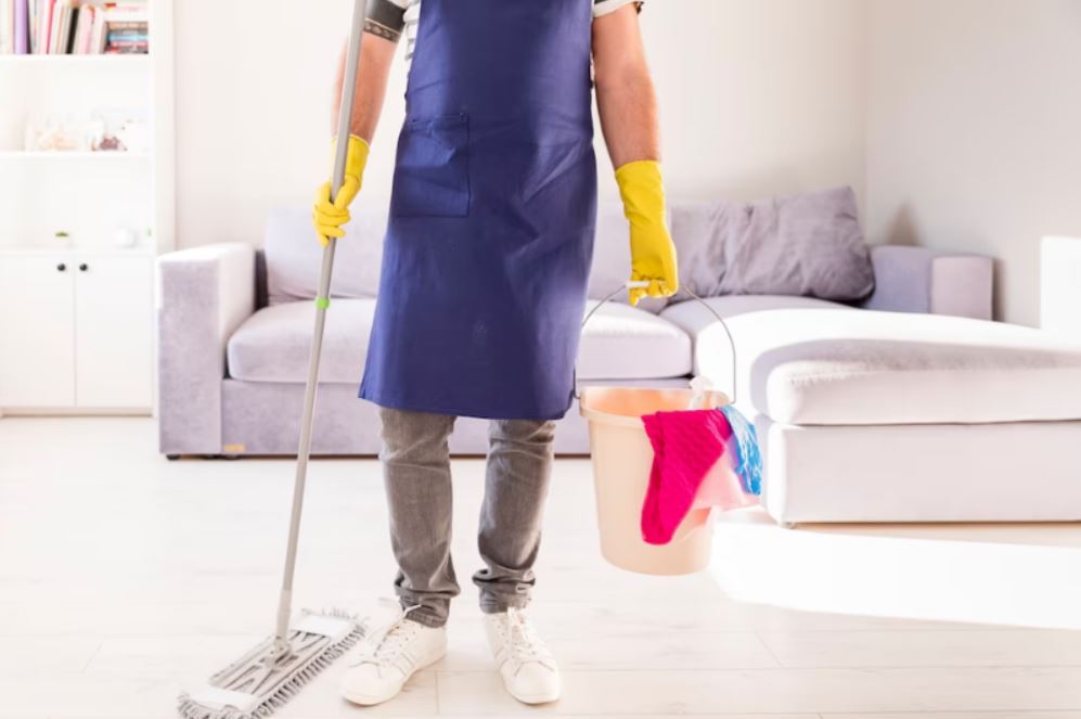 Een professionele schoonmaker met een dweil en een emmer met schoonmaakdoeken tonen bank reinigen in Bloemendaal